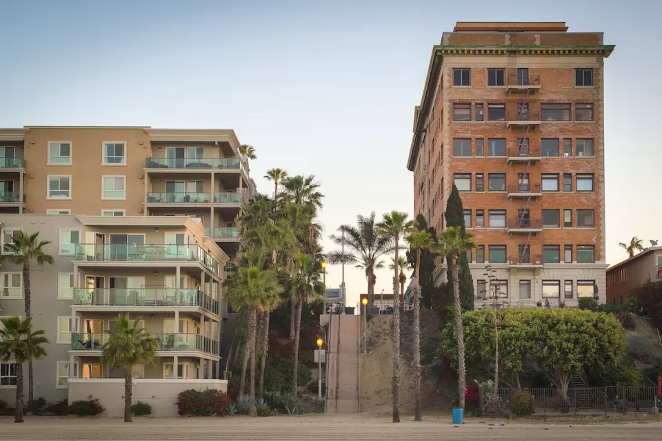 Vintage multi-story brick apartment building and modern concrete and glass apartment building separated by a steep public stairway in Los Angeles, California.